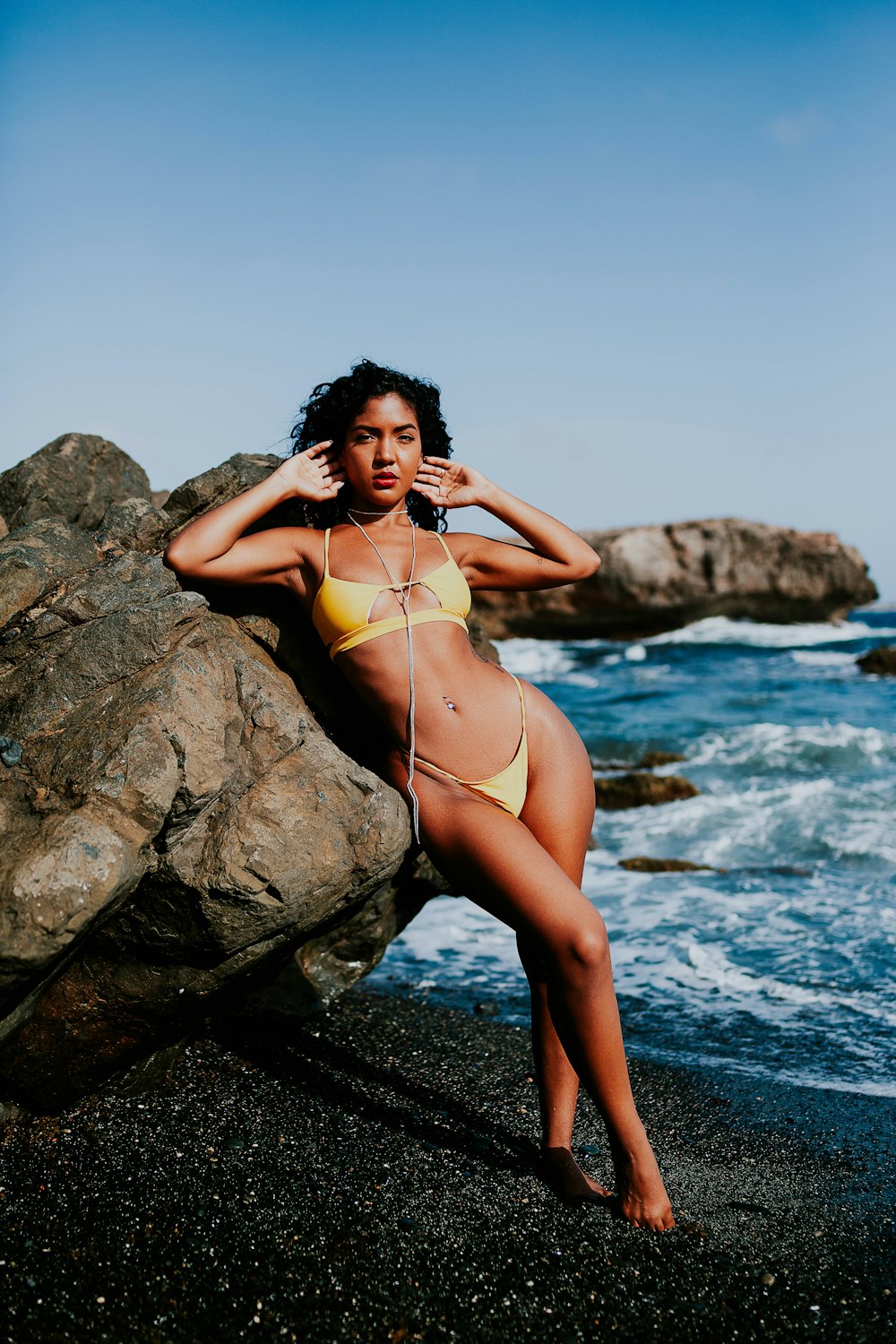 woman in yellow bikini standing on rock near body of water during daytime