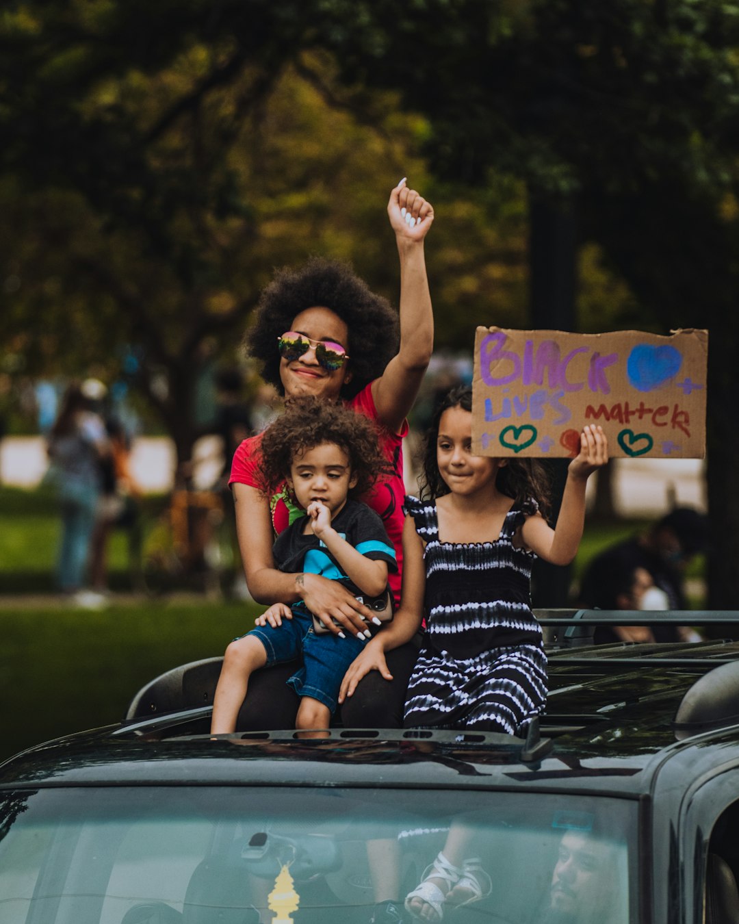 2 women sitting on black car during daytime