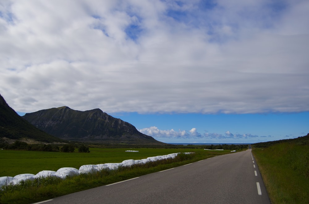 gray concrete road near green grass field under white clouds and blue sky during daytime