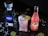 A bottle of 1800 Silver Tequila, an ice-filled crystal glass with a frothy pink drink garnished with a lime slice, and a bottle of Jarritos Guava soda are placed on a dark surface. Lime slices and white shredded pieces are scattered around.