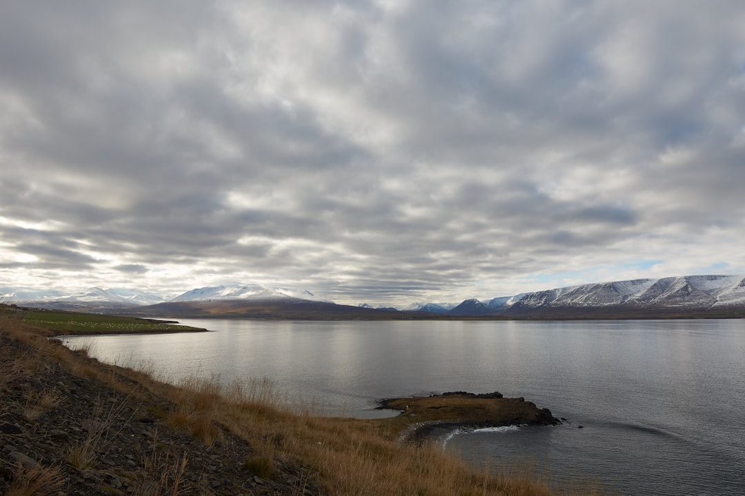 body of water near mountain under cloudy sky during daytime