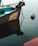 A small boat is moored in calm water, with a visible anchor chain extending to a buoy floating nearby. The boat is named, and part of its aqua-colored interior can be seen, along with a motor attached at the stern.