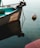 A small boat is moored in calm water, with a visible anchor chain extending to a buoy floating nearby. The boat is named, and part of its aqua-colored interior can be seen, along with a motor attached at the stern.