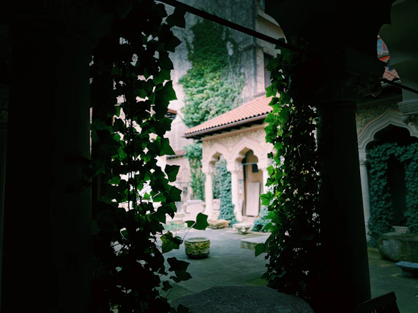 Sunlit seminary courtyard with soft greenery and morning light filtering through traditional wooden pillars.