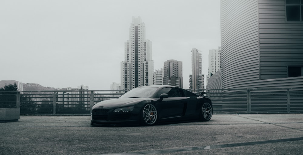 Porsche 911 nera parcheggiata sul marciapiede grigio vicino agli edifici della città durante il giorno