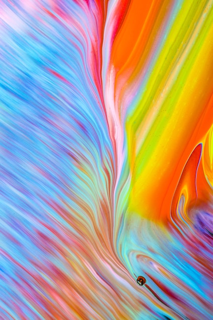 A vibrant blend of swirling colors including blue, purple, red, orange, yellow, and green. The abstract design has a fluid, dynamic motion, resembling pigments mixing or flowing together. The colors are saturated and create a visually stimulating pattern with varied intensities.