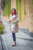A vibrant street style photo featuring a woman in a sage green trench coat walking past a lavender-painted wall.