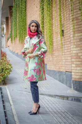 A vibrant street style photo featuring a woman in a sage green trench coat walking past a lavender-painted wall.