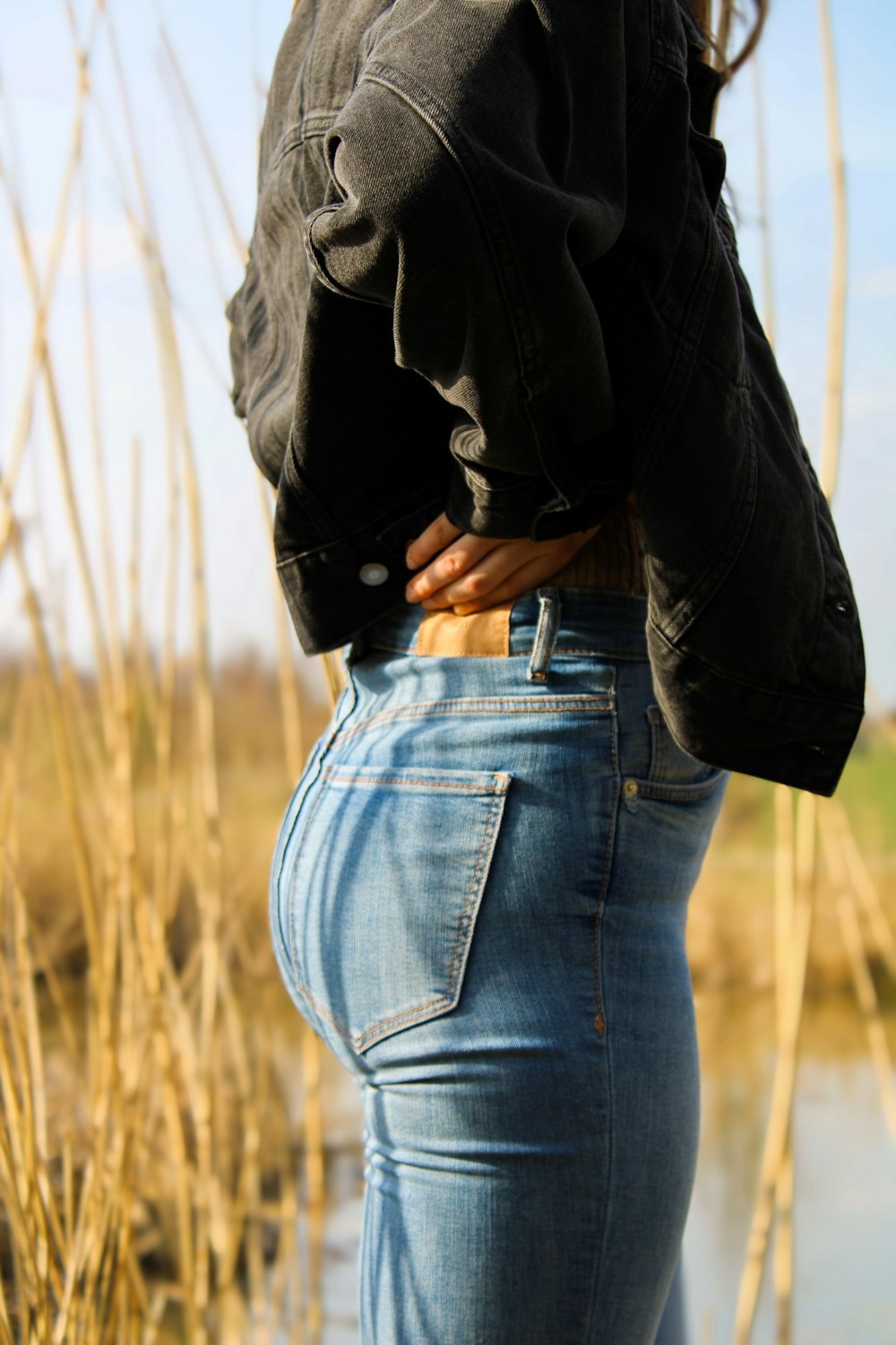 Persona con chaqueta negra y jeans de mezclilla azul de pie en el campo de hierba durante el día