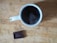 A steaming cup of dark coffee is placed on a wooden surface, accompanied by a piece of dark chocolate nearby.