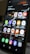 A close-up view of a smartphone screen displaying various application icons including Office, Teams, Camera, Messenger, Gmail, YouTube, and more. The background contains a reflection of an interior space with lighting and signage. There are also notifications and health data displayed at the top of the screen.