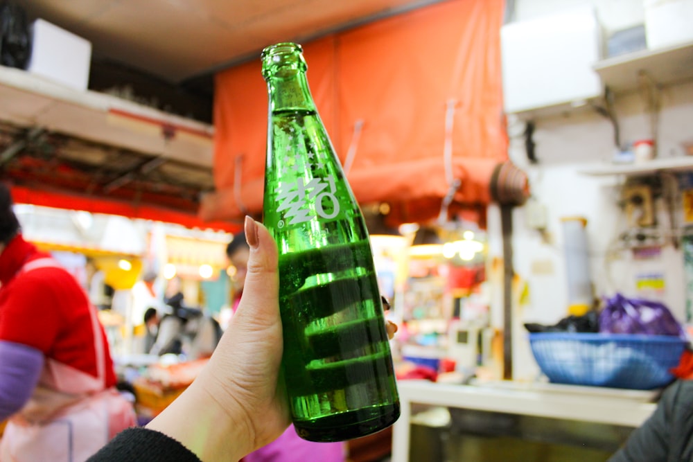 person holding green glass bottle