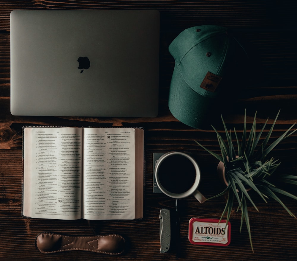 Offenes Buch neben schwarz-roter Digitaluhr und silbernem MacBook