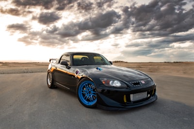 black porsche 911 on brown sand under gray clouds emotionally charged zoom background