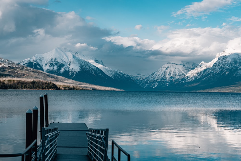 brown wooden dock on lake near snow covered mountain