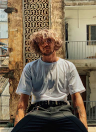 man in white crew neck t-shirt sitting on brown concrete wall during daytime