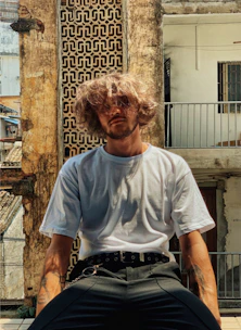 man in white crew neck t-shirt sitting on brown concrete wall during daytime