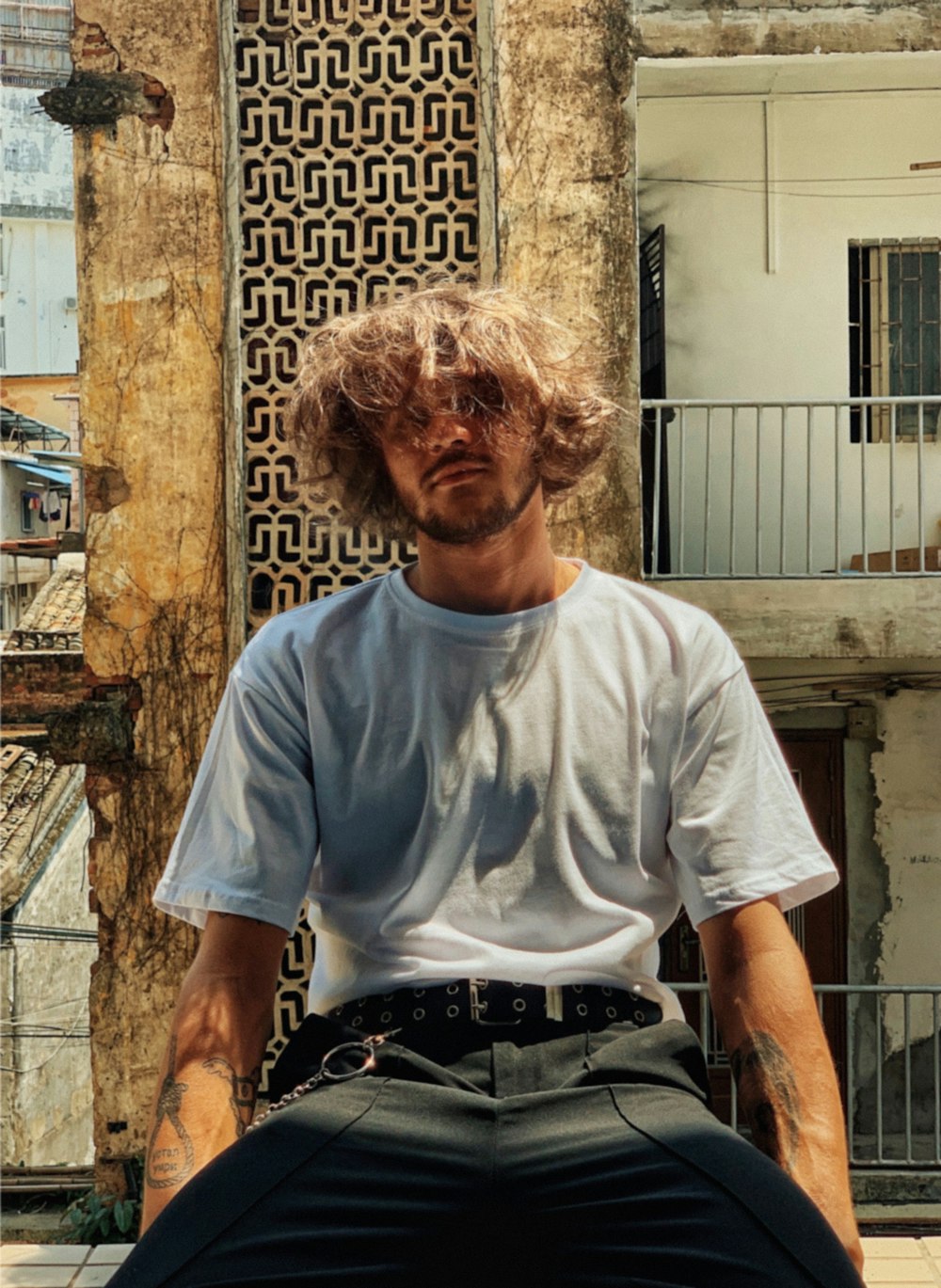 man in white crew neck t-shirt sitting on brown concrete wall during daytime