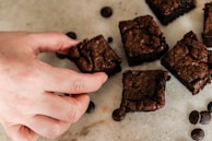 A hand breaking a warm brownie, showing its gooey texture inside.