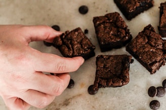 A hand breaking a warm brownie, showing its gooey texture inside.