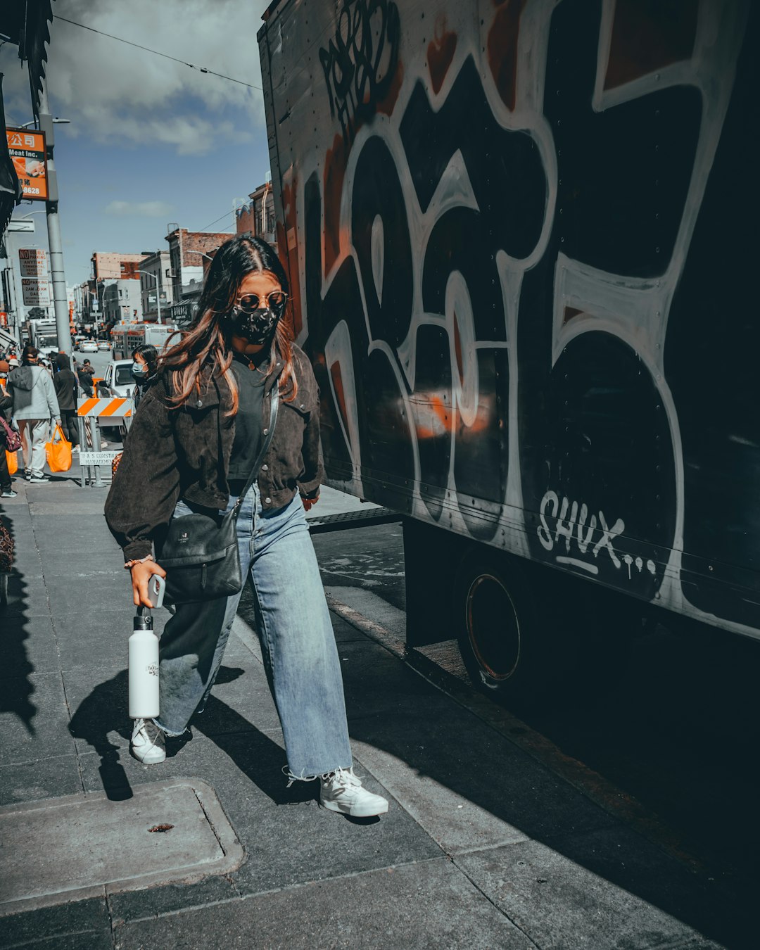 woman in black jacket and blue denim jeans walking on pedestrian lane during daytime