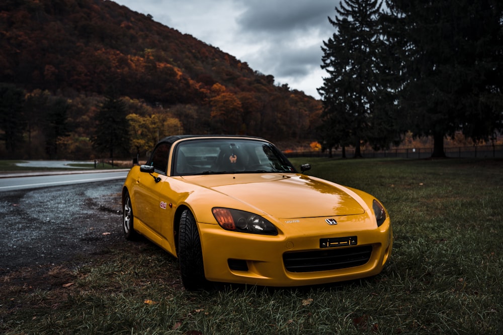 Porsche 911 amarillo en un campo de hierba verde cerca de la montaña durante el día