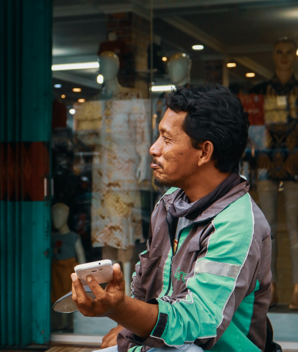 man in white and green jacket holding white smartphone