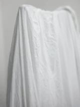 Softly lit photo of a handcrafted feminine garment hanging against a neutral background.