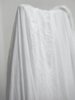 Softly lit photo of a handcrafted feminine garment hanging against a neutral background.