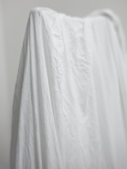A soft, draped fabric in neutral tones hanging gracefully on a minimalist backdrop.