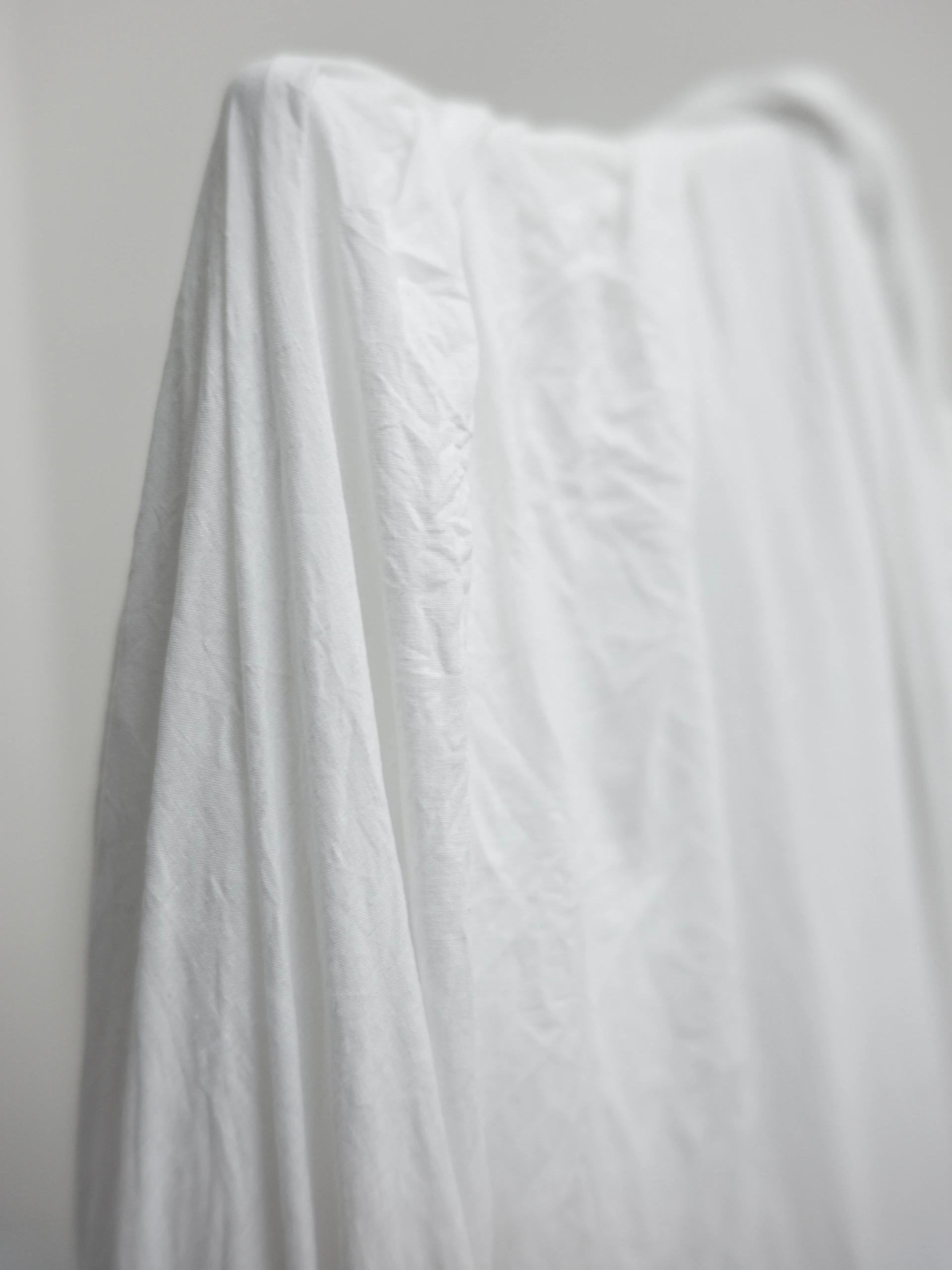 Close-up of a textured, high-quality fabric of a minimalist white beach cover-up, draped over a sunlit sandy shore.