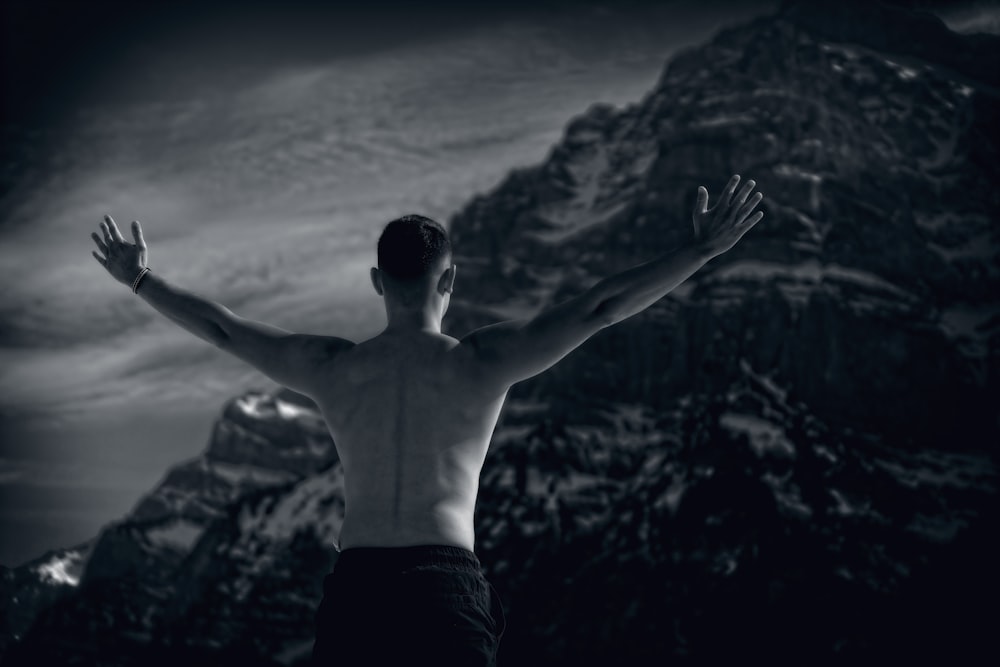 topless man in black shorts standing on rock formation