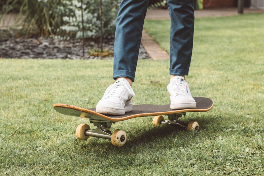 person in blue denim jeans and white sneakers riding brown skateboard on green grass field during