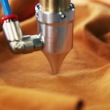 A metal nozzle attached to a blue and red tube presses against a piece of orange fabric.