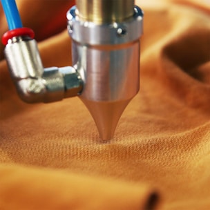 Bright orange adhesive being sprayed onto mattress fabric.