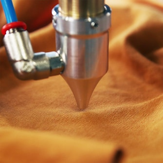 A metal nozzle attached to a blue and red tube presses against a piece of orange fabric.