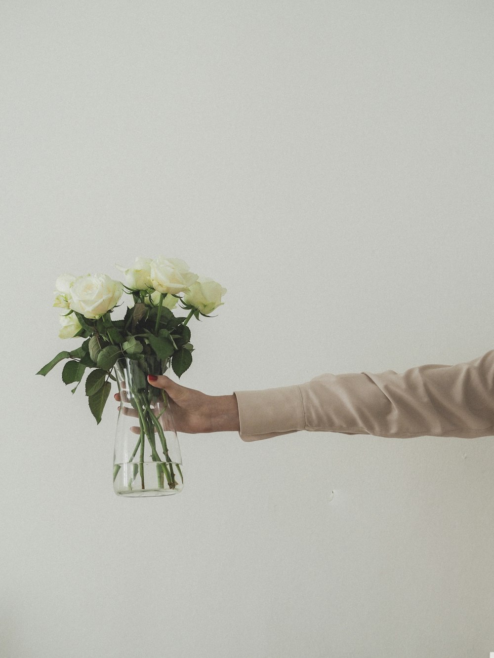 person holding white and yellow flowers in clear glass vase