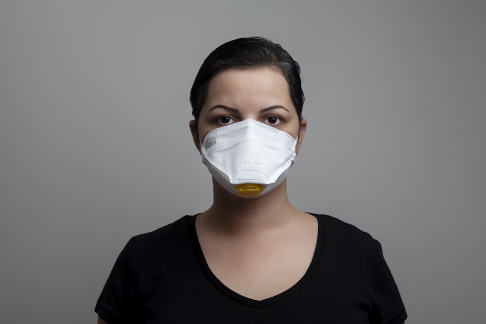 白いフェイスマスクを着用する黒いクルーネックシャツの女性