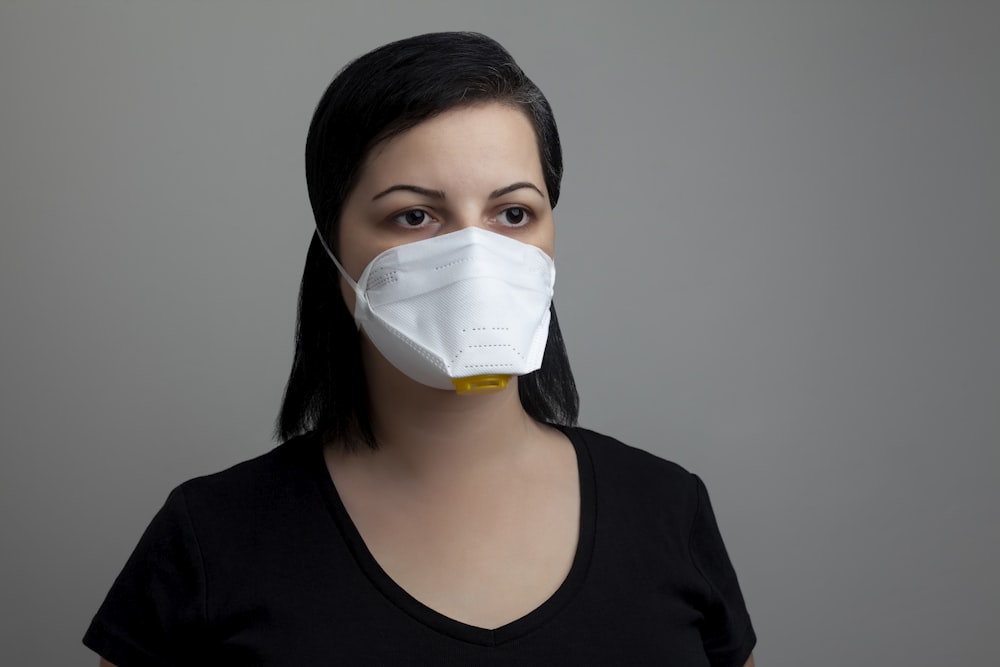 Mujer con camisa negra de cuello redondo con mascarilla blanca