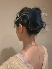 A person with dark hair is styled in an elegant updo adorned with intricate silver accessories. The individual wears a delicate lace garment, revealing the upper back and neck. The background is neutral, emphasizing the focus on the hairstyle and accessories.