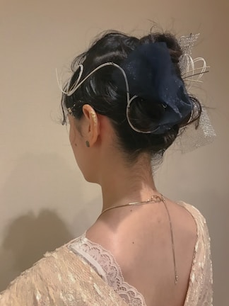 A person with dark hair is styled in an elegant updo adorned with intricate silver accessories. The individual wears a delicate lace garment, revealing the upper back and neck. The background is neutral, emphasizing the focus on the hairstyle and accessories.