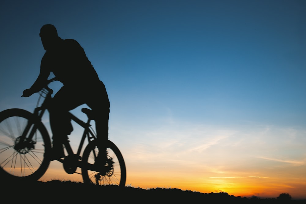 silhouette of man riding bicycle during sunset