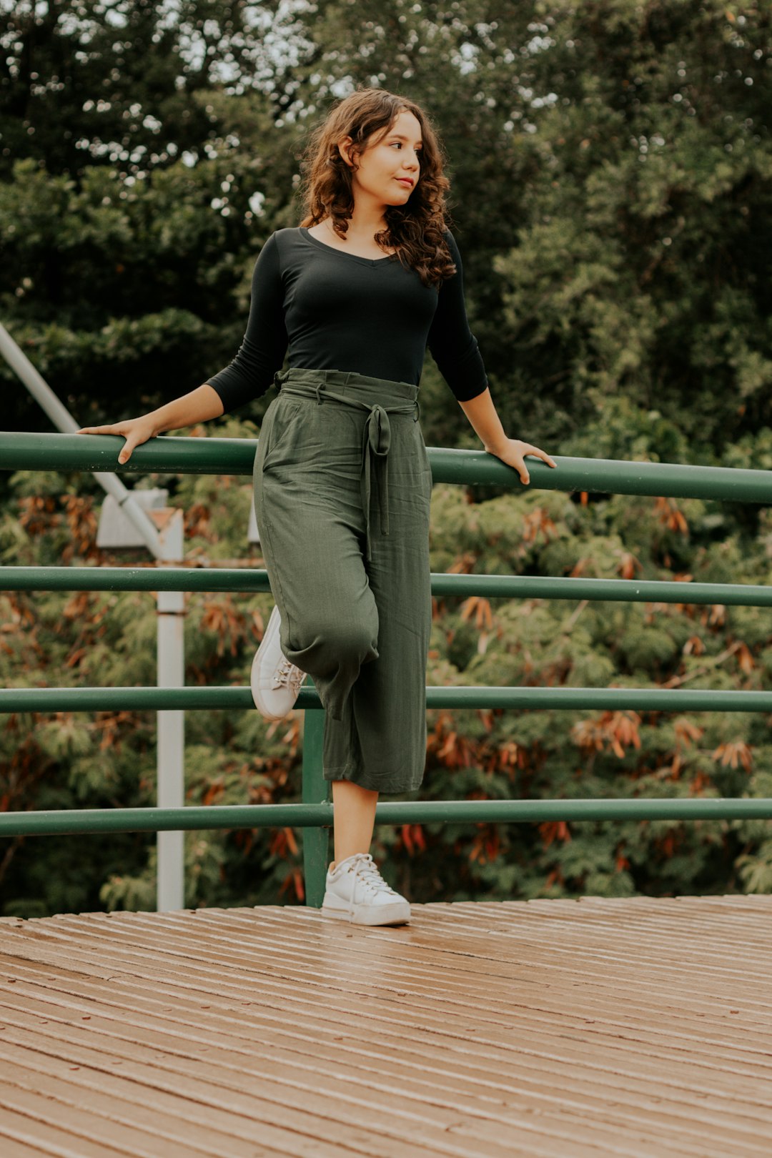 woman in black long sleeve shirt and gray pants standing on brown wooden bridge during daytime