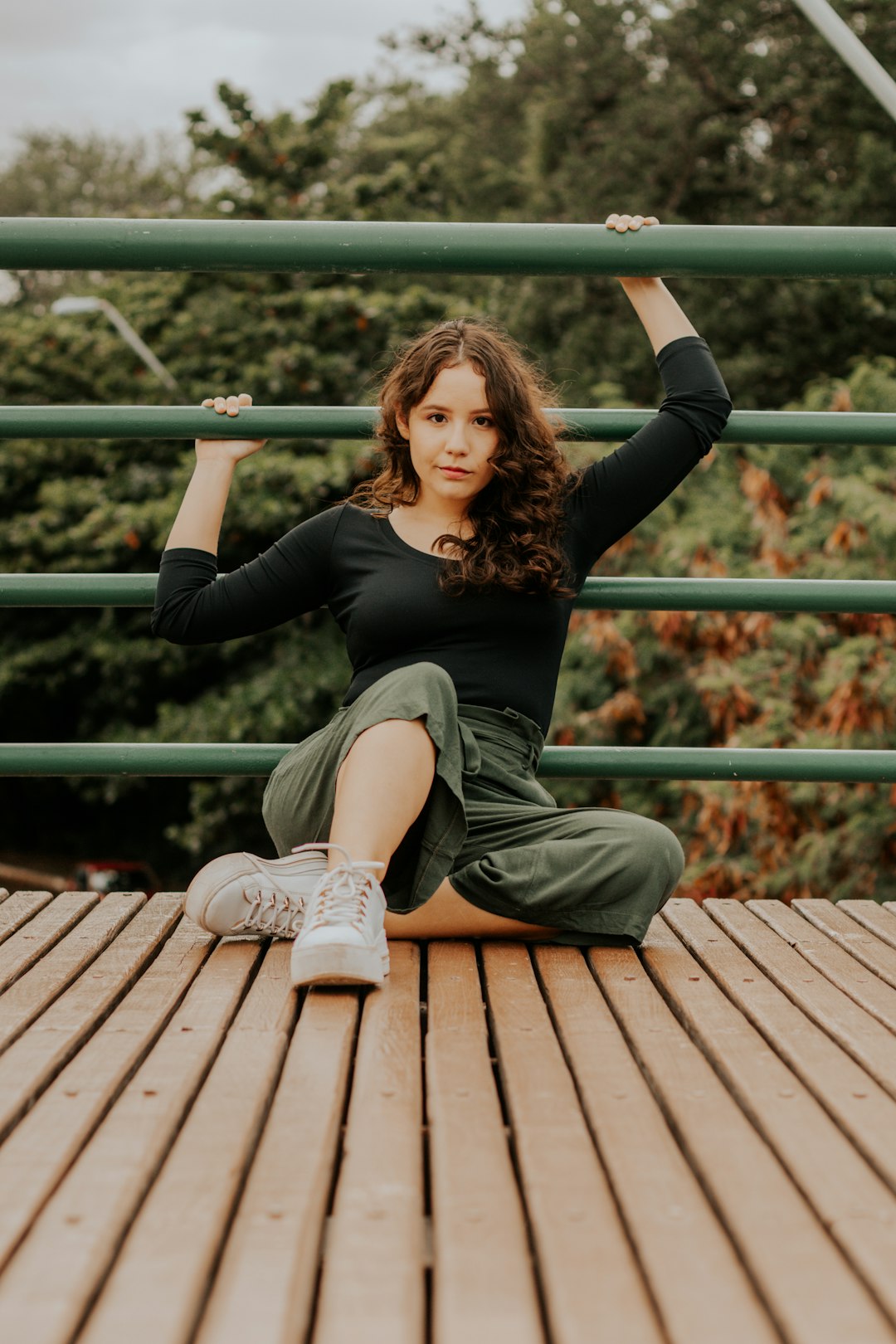 woman in black long sleeve shirt and gray pants sitting on brown wooden bridge during daytime