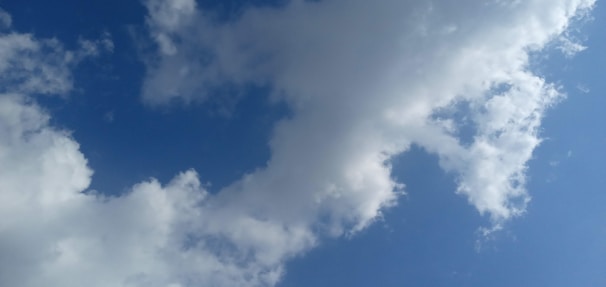 White clouds scattered across a clear blue sky, with sunlight illuminating the edges of the clouds, creating soft shadows and highlights.