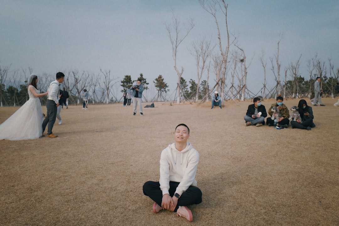 man in white long sleeve shirt sitting on brown field during daytime