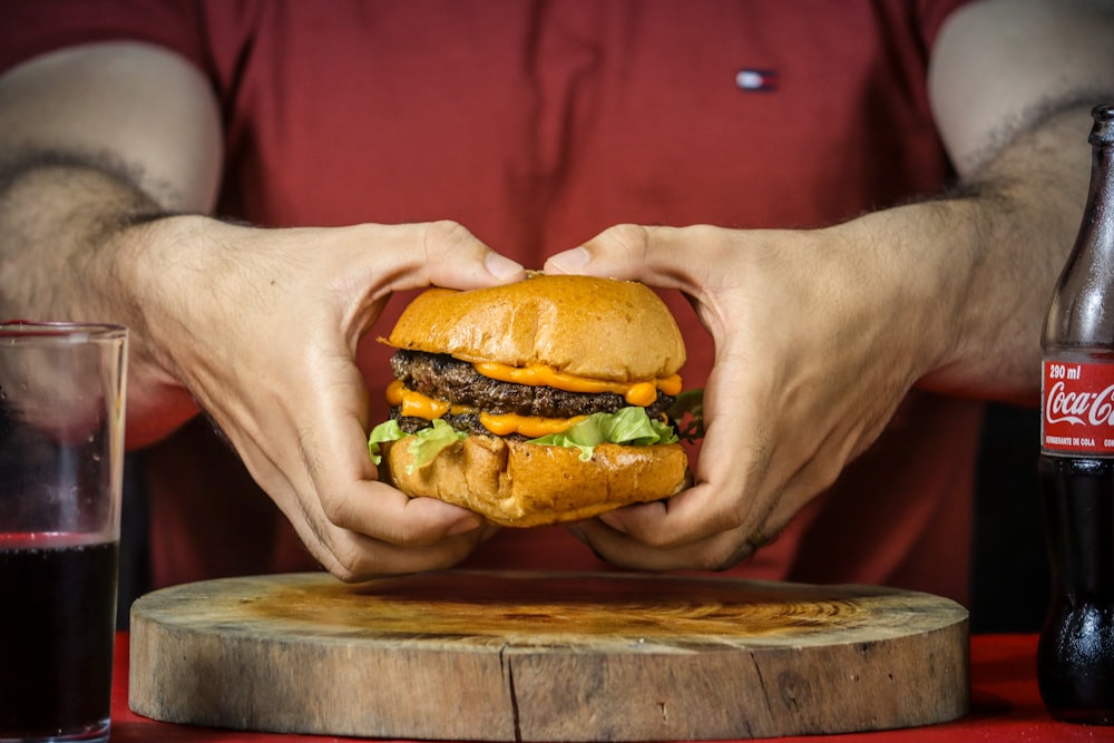 person holding burger with cheese and lettuce
