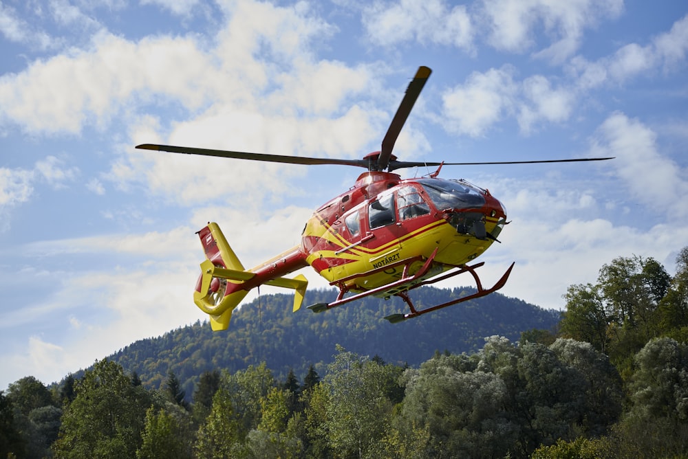 red and yellow helicopter flying over green trees during daytime