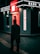 A person walks past a modern, illuminated bank kiosk in an urban setting. The signage is prominently displayed with the name 'Bank Maskan' in bright red and white colors. The atmosphere is dark with artificial lighting creating a contrast against the surroundings.