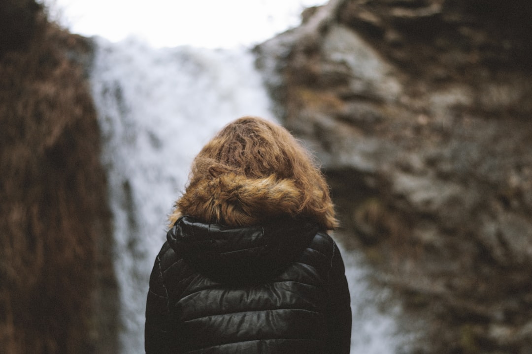 person in black parka jacket standing near gray rock formation during daytime